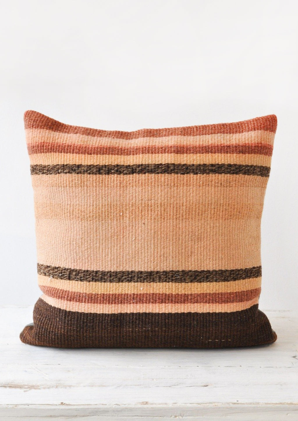 1: A striped kilim pillow in rust, adobe, and brown.