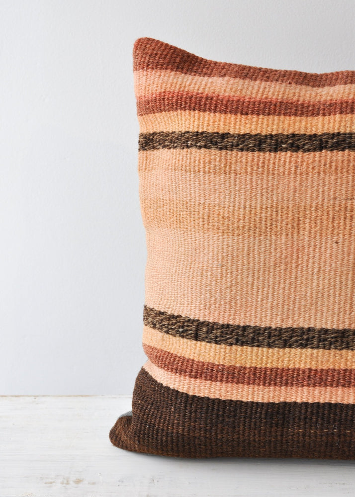 A closeup of a stripe kilim pillow in rust, adobe, and brown. 