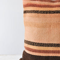 3: A closeup of a stripe kilim pillow in rust, adobe, and brown. 