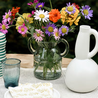 3: A clear, jug-shaped glass vase on a set table with flowers.