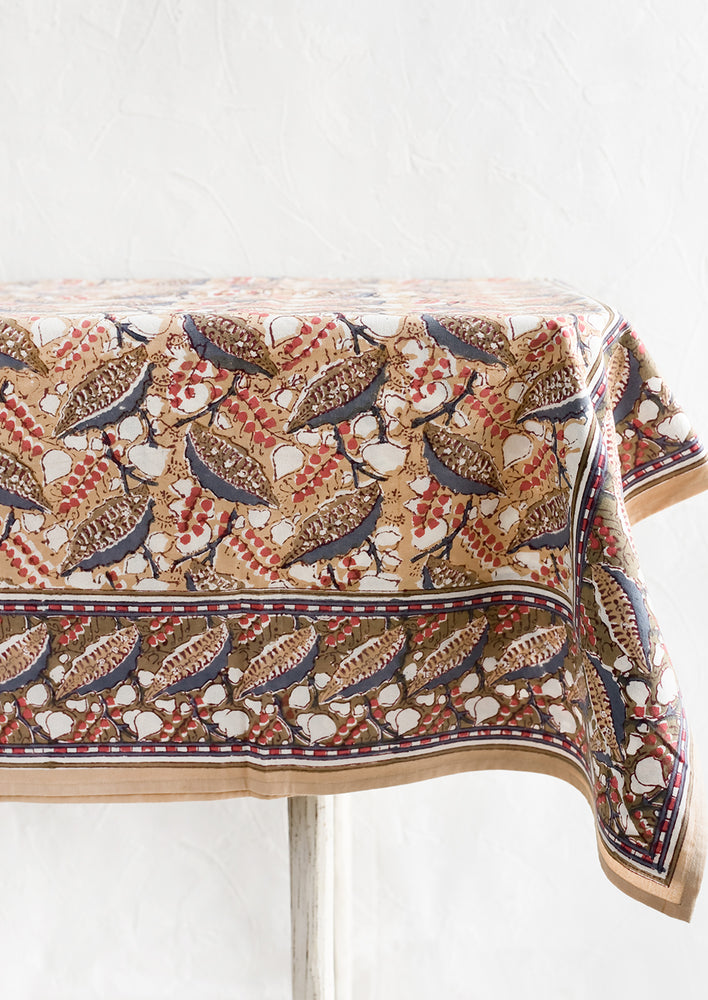 1: A block print tablecloth with tan, red and slate blue floral print.