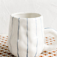 3: A pinched white mug with vertical thin blue stripes.