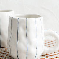 2: A pinched white mug with vertical thin blue stripes.