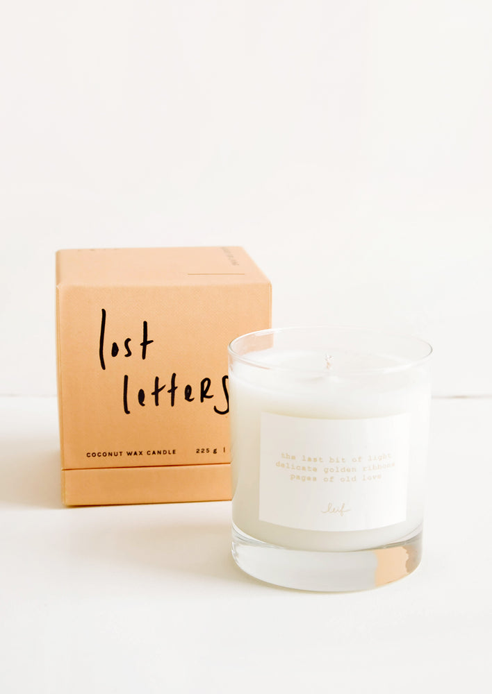 A glass candle with a white label sits next to a peach colored box reading "lost letters" in black cursive text.