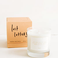 Lost Letters: A glass candle with a white label sits next to a peach colored box reading "lost letters" in black cursive text.