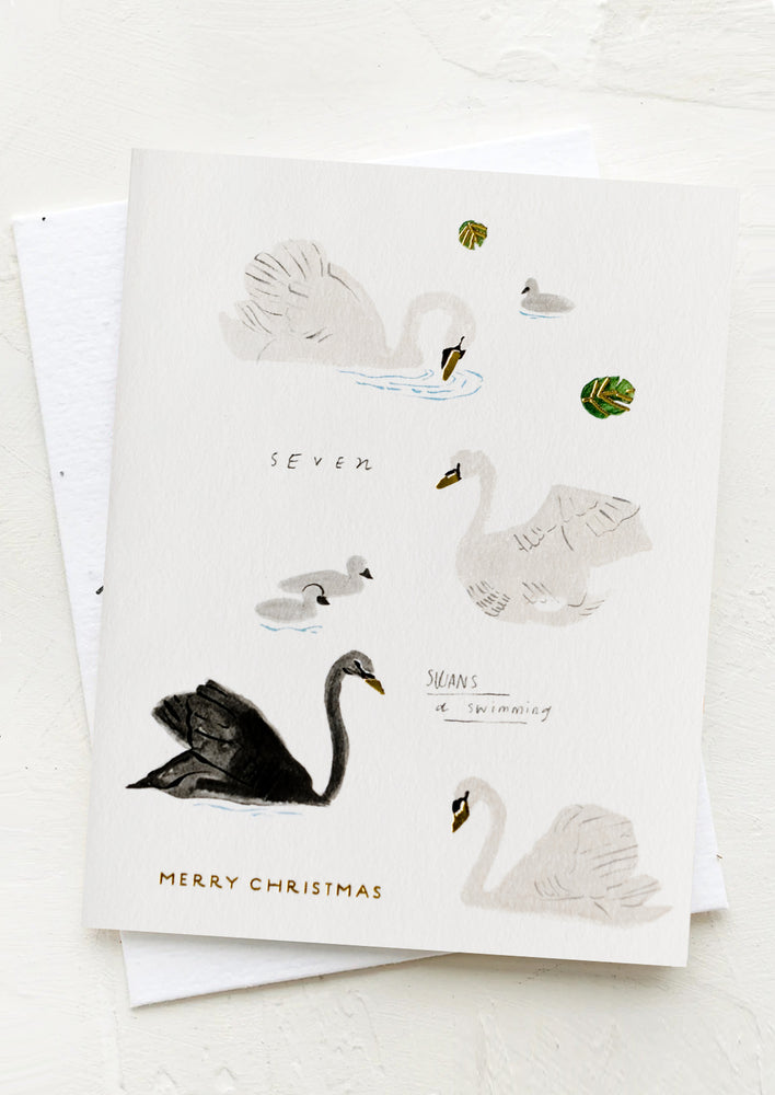 A card with illustrations of swans, text reads "seven swans a swimming, merry christmas".