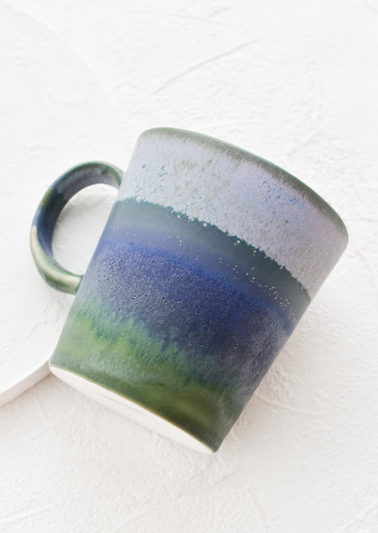 A ceramic coffee mug with handle in mottled blue and green glaze.