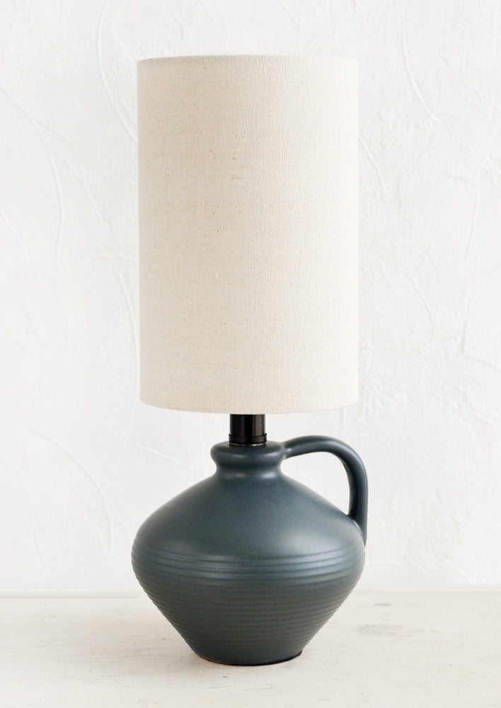 A table lamp with charcoal ceramic base and cylindrical natural cotton shade.