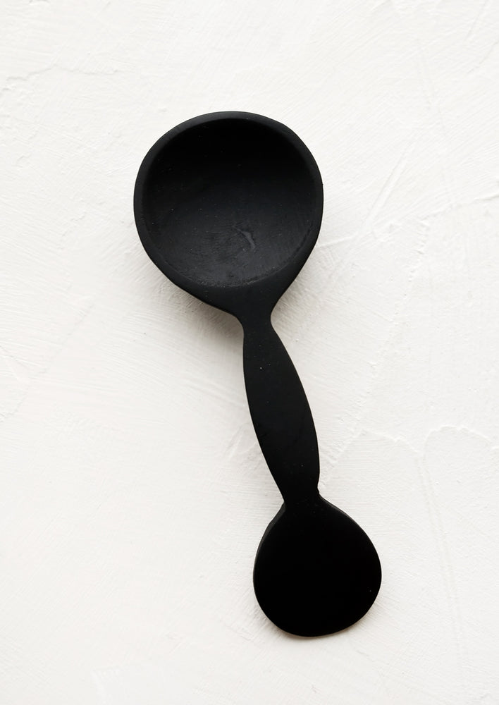 A carved black wooden teaspoon with decorative circular handle.