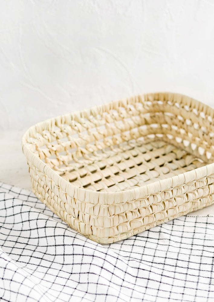 A shallow storage basket made from dried palm leaf.