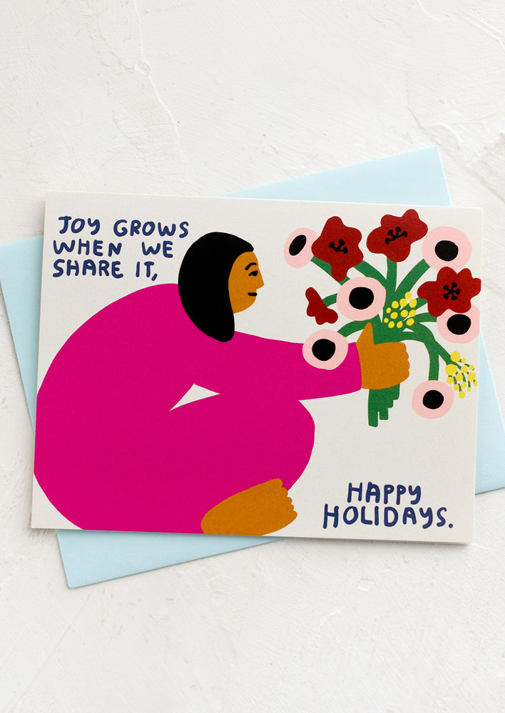 A card with drawing of woman holding a bouquet of flowers, text reads "Joy grows when we share it, happy holidays".