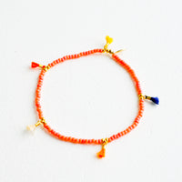 Red Coral: Bracelet featuring red beads interspersed with 5 small multicolor string tassels on an elastic cord.