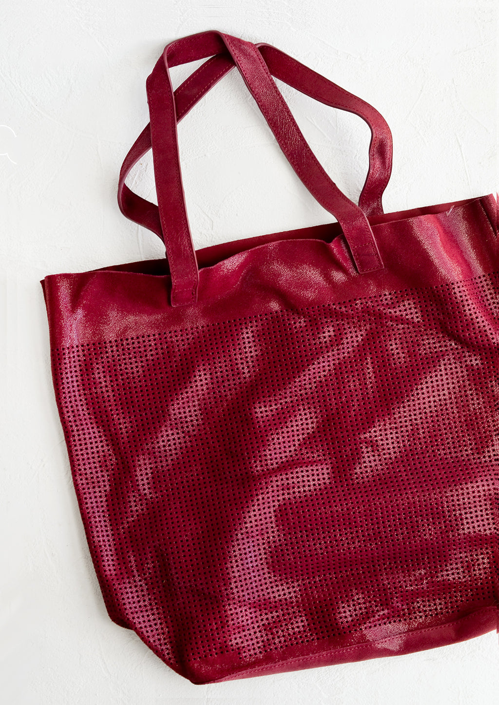 Cranberry: A tote bag made from cranberry colored shimmer leather with square perforation detailing throughout.