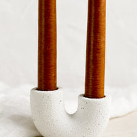1: A white jesmonite taper holder holding rust colored taper candles.