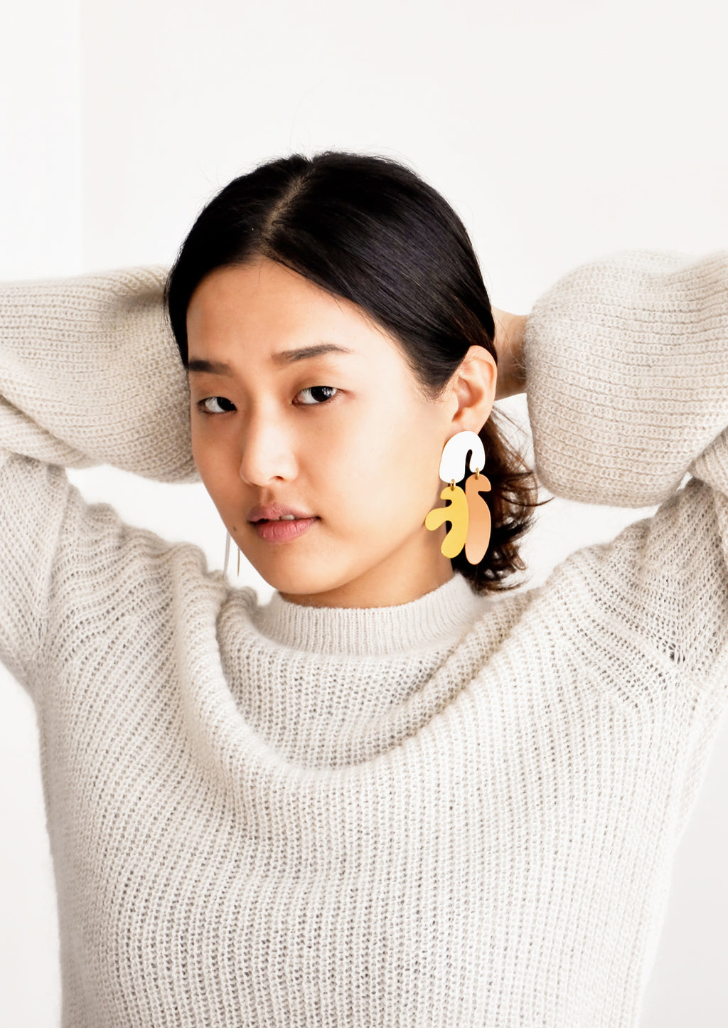 2: Model shot of woman wearing earrings and white sweater.