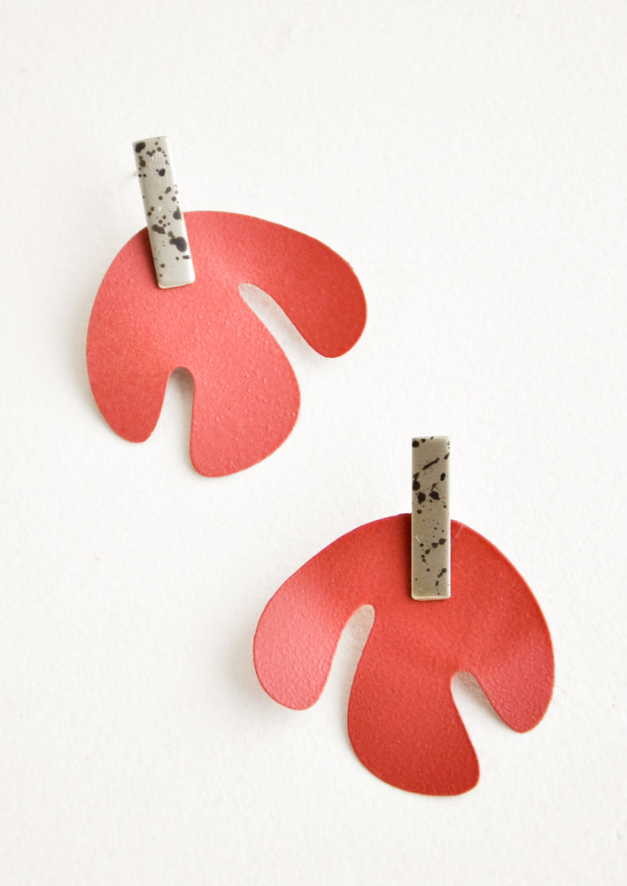 Post earrings with red asymmetric leaf shape hanging from small speckled rectangle.
