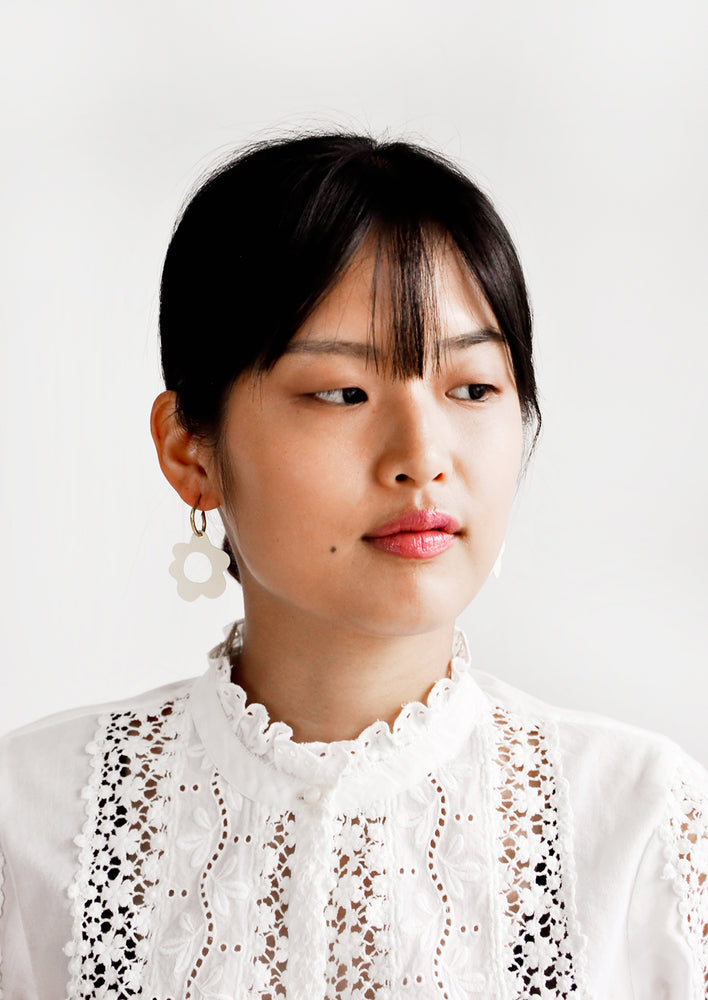 Model wears white flower-shaped earrings and white blouse.