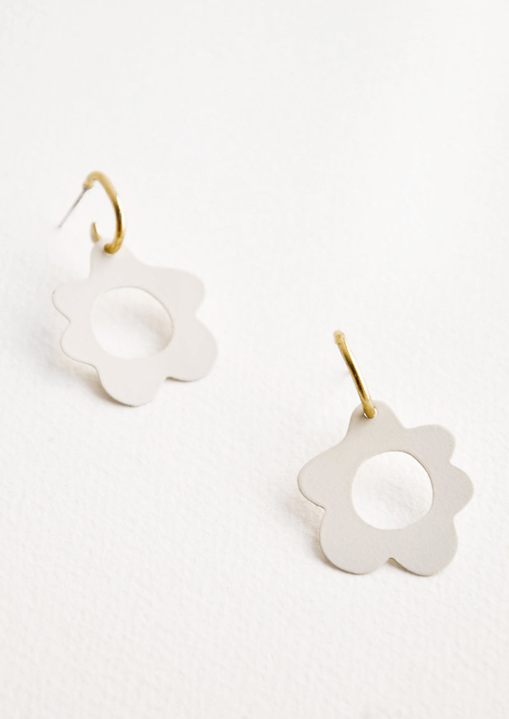 Cream: White flower shaped earrings with circular cutouts on small brass open hoops.