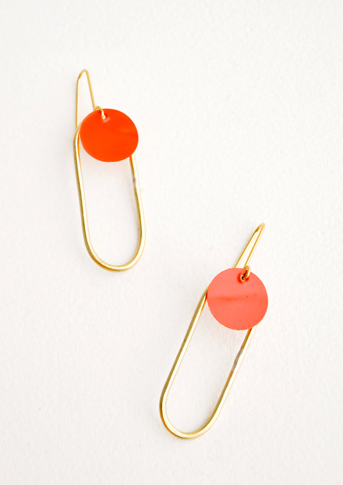Pair of earrings in the shape of a hollow brass oval with a red dot at the top. 