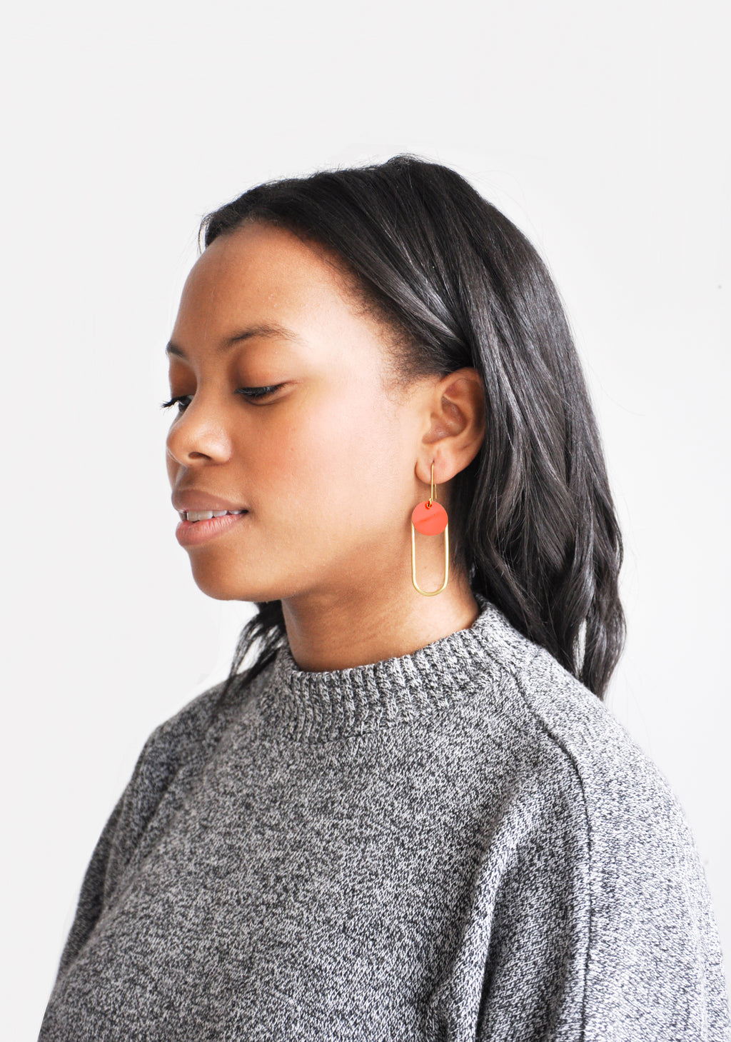 2: Woman modeling geometric, oval-shaped brass and enamel earrings.