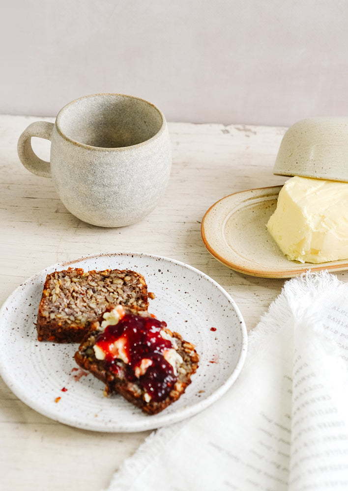 A breakfast tableware scene with coffee mug, butter dish and toast and jam on a ceramic plate.