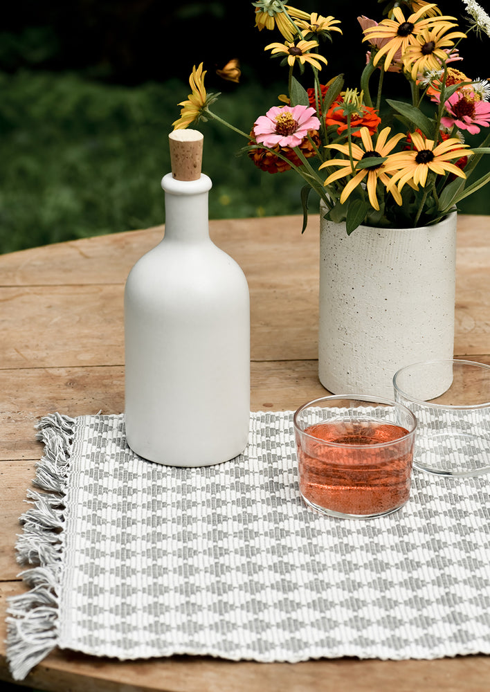 A placemat on table with white bottle and vase of flowers.