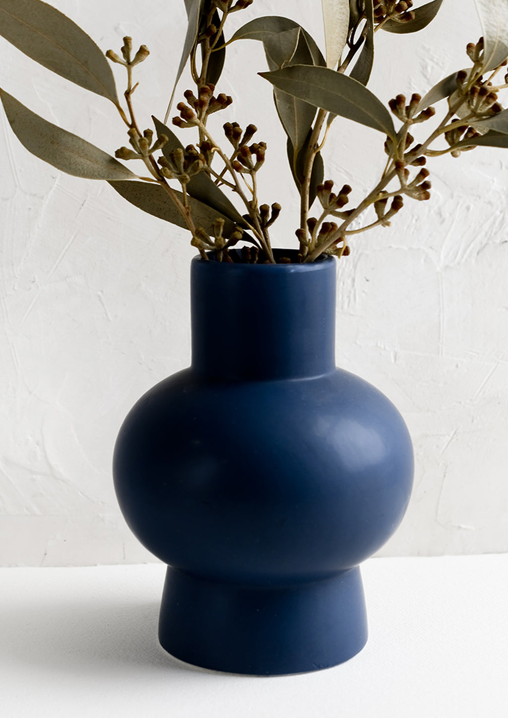 2: A navy blue sculptural ceramic vase with dried eucalyptus.