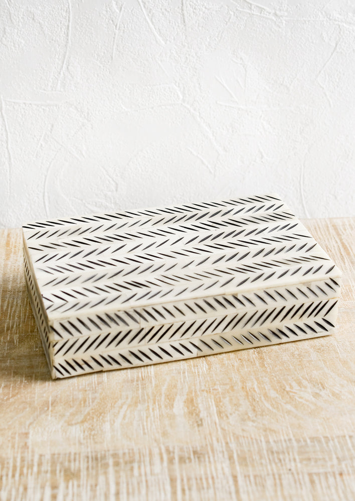 A decorative storage box made from ivory bone with black etched "slash" pattern.