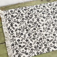 1: A black and white floral print placemat with fringe trim.