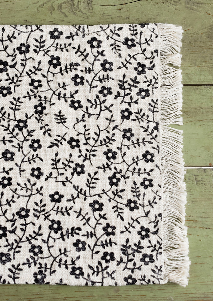 3: A black and white floral print placemat with fringe trim.