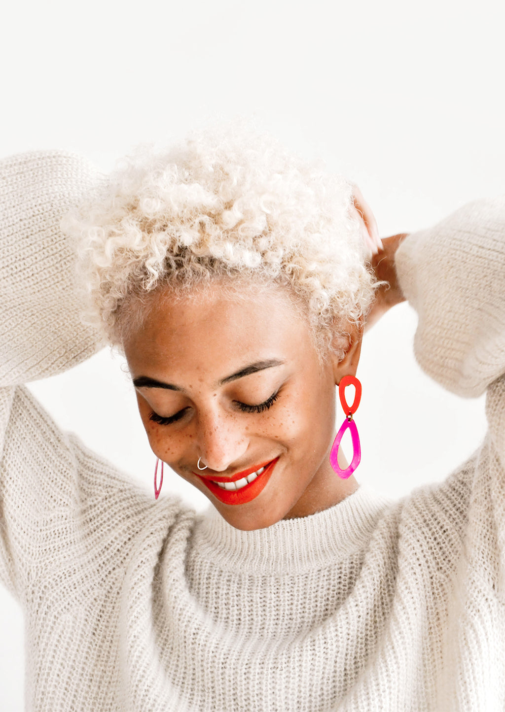 2: Model wears vibrant coral and fuchsia drop earrings and ivory sweater.