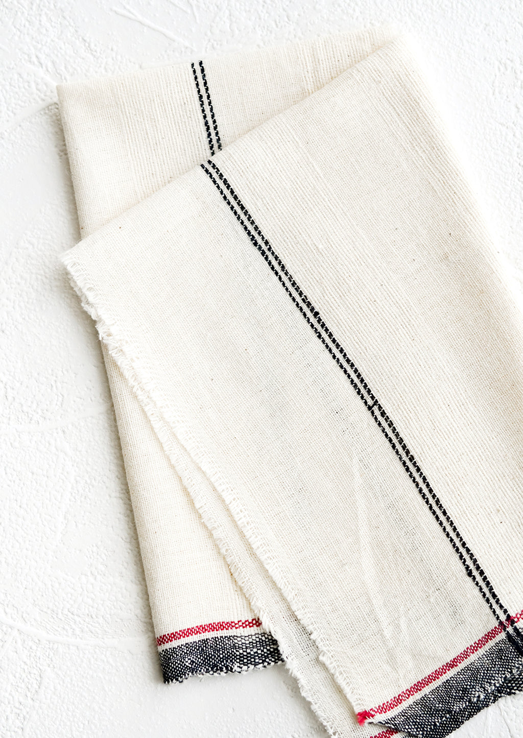2: A natural cotton napkin with black and red stripe detailing and raw edges.