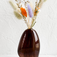 2: An asymmetrical bud vase in brown colored glass, holding dried flowers.