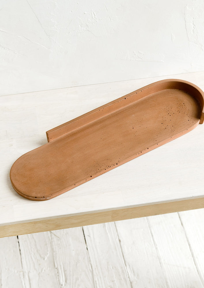 An elongated oval shaped platter made from rust colored concrete.