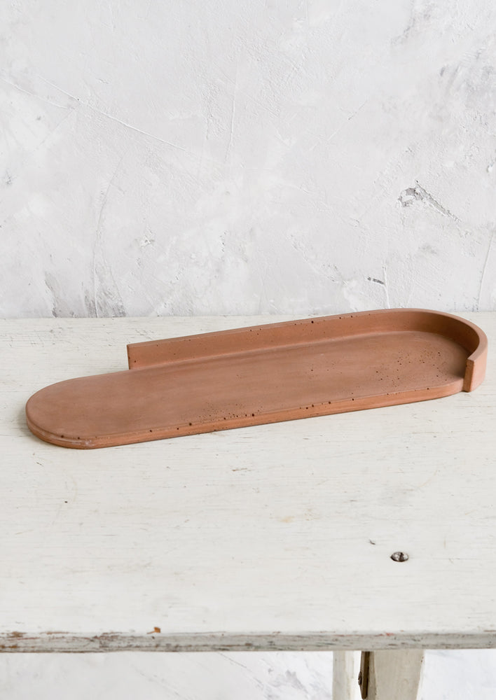An elongated oval shaped platter made from rust colored concrete.