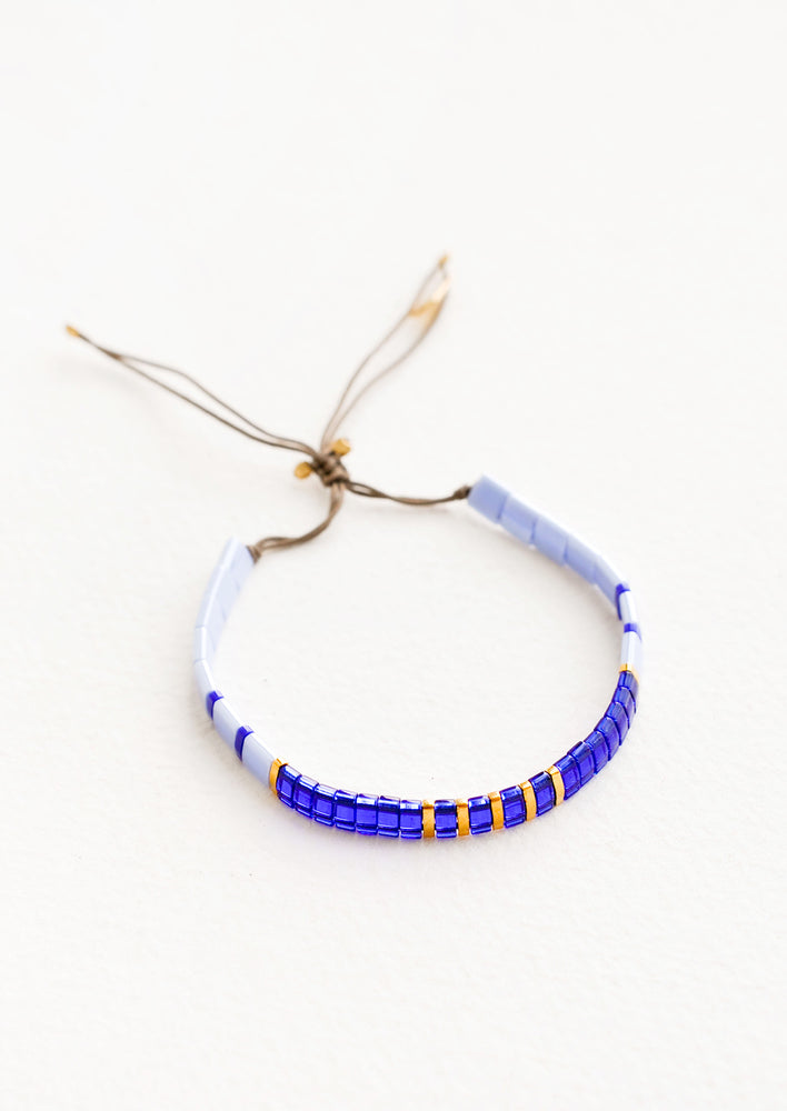 Blue: Bracelet featuring flat multicolor blue glass beads interspersed with flat gold bead on an adjustable cord.