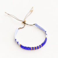 Blue: Bracelet featuring flat multicolor blue glass beads interspersed with flat gold bead on an adjustable cord.