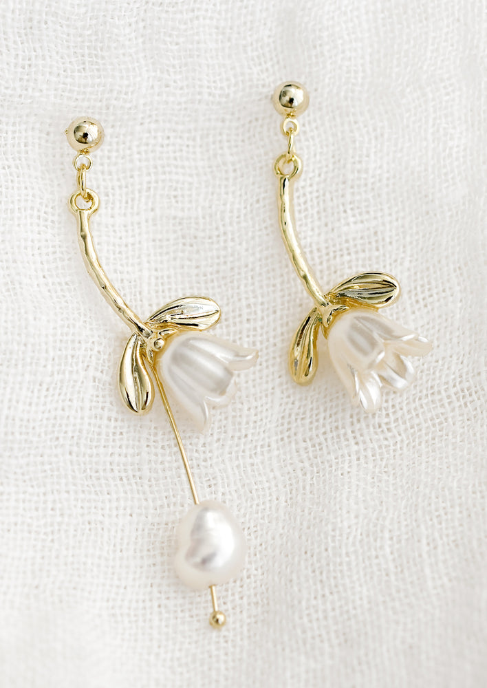 A pair of mismatched earrings with snowdrop and pearl design.
