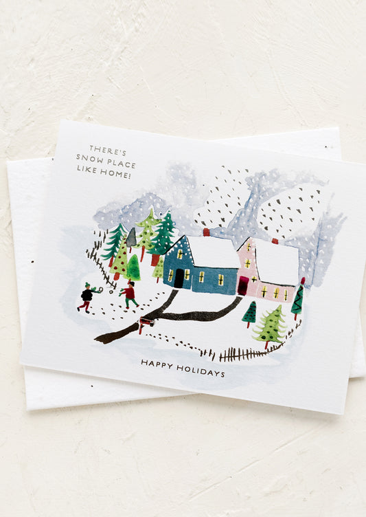 A greeting card with snowy village illustration, text reads "There's Snow Place Like Home!".