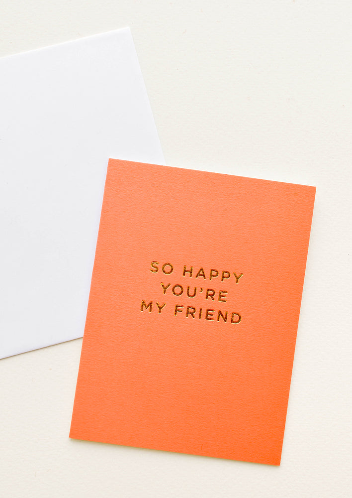 1: A white envelope and orange greeting card with the words "so happy you're my friend" in gold foil.