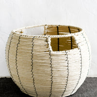 2: A round belly shaped basket in natural cord with thin black vertical stripe.