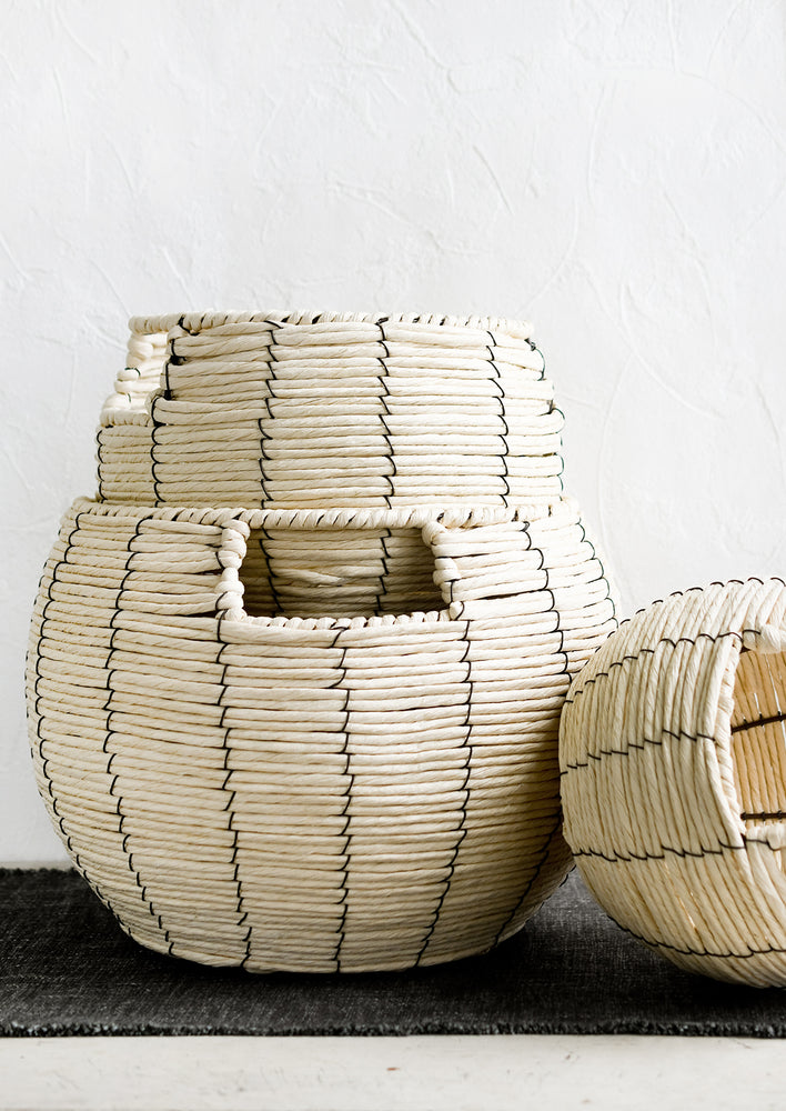 A round belly shaped basket in natural cord with thin black vertical stripe.