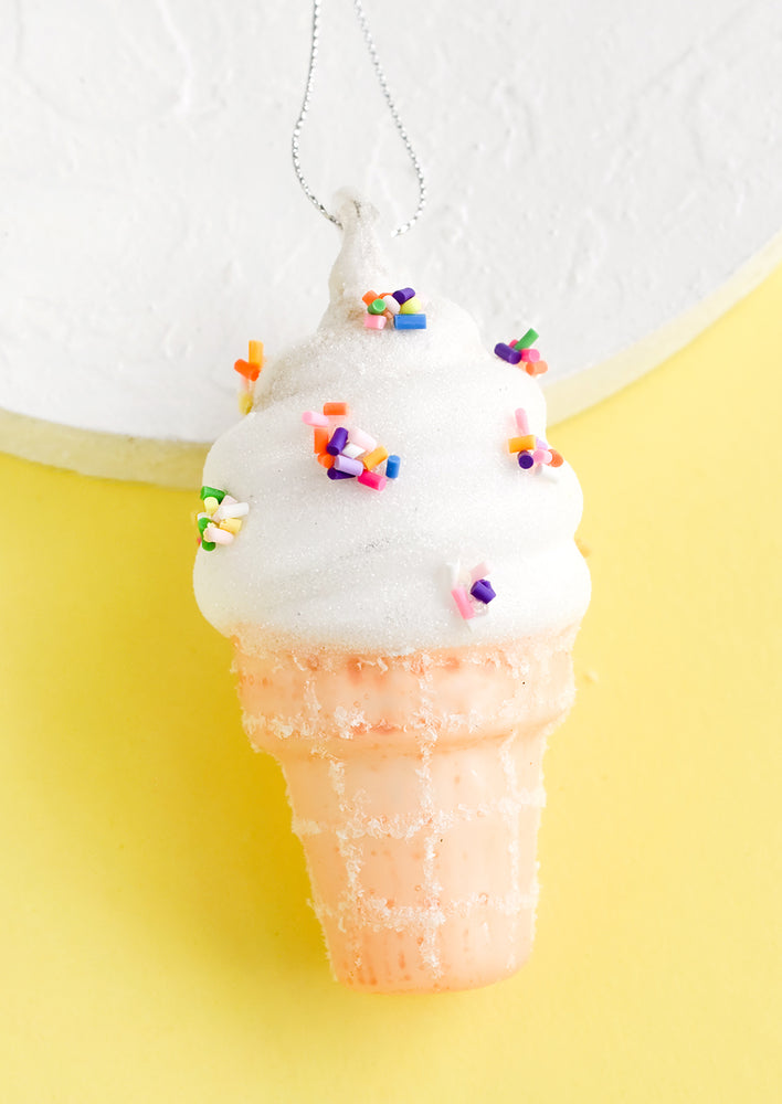 A glass ornament in shape of vanilla soft serve ice cream cone with sprinkles.