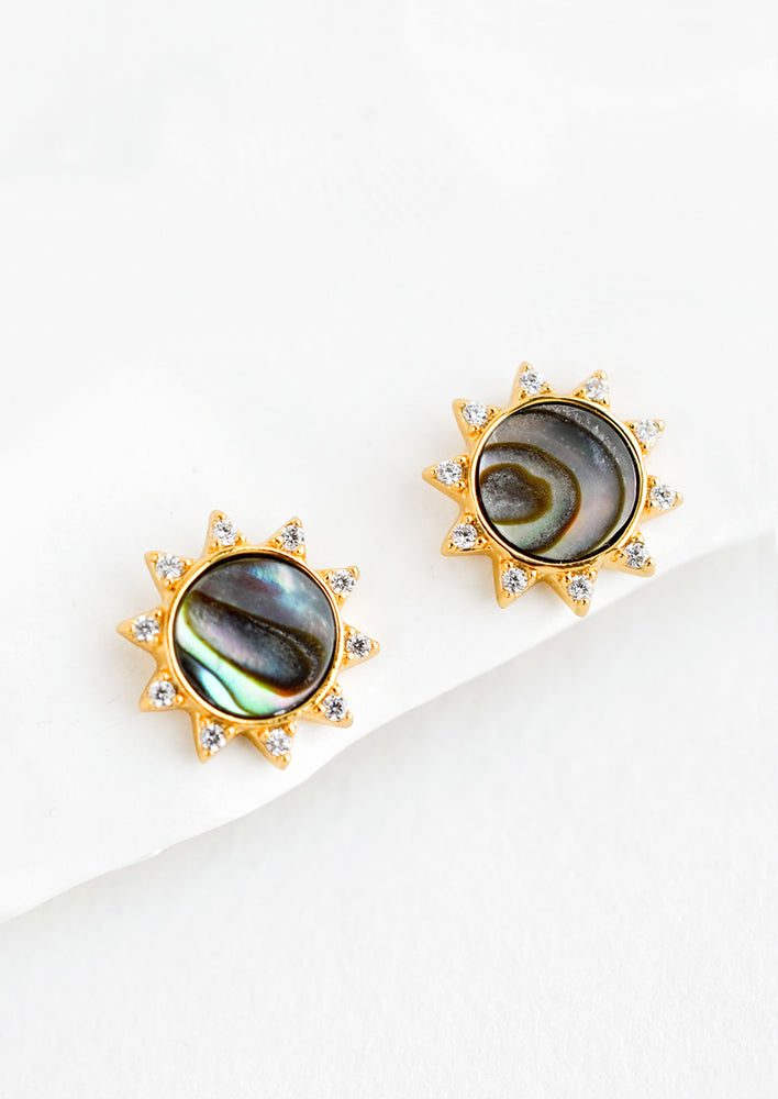 A pair of gold stud earrings in the shape of a sun with shell inlay center and crystal "sunray" border.