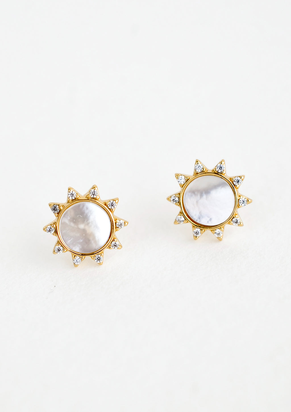 Mother of Pearl: A pair of gold stud earrings in the shape of a sun with shell inlay center and crystal "sunray" border.