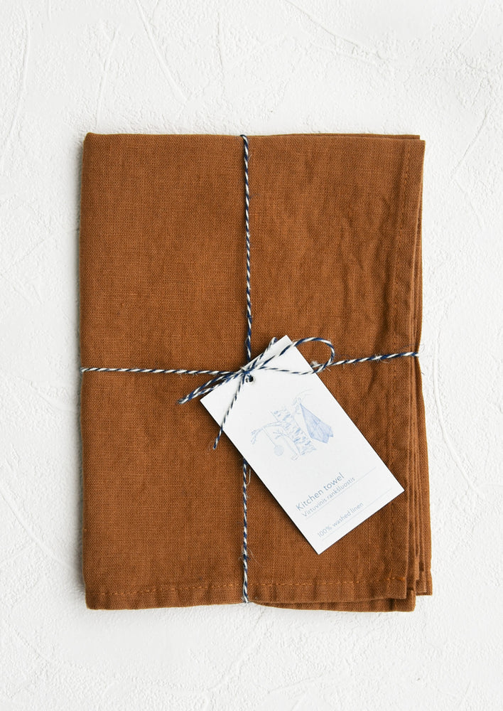 A folded rust color linen tea towel tied in baker's twine with a decorative hangtag