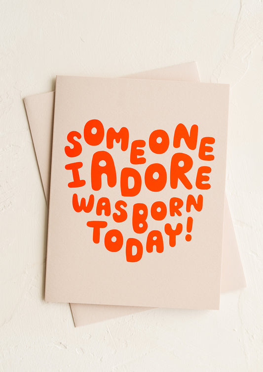 A tan greeting card with red letters in heart shape.