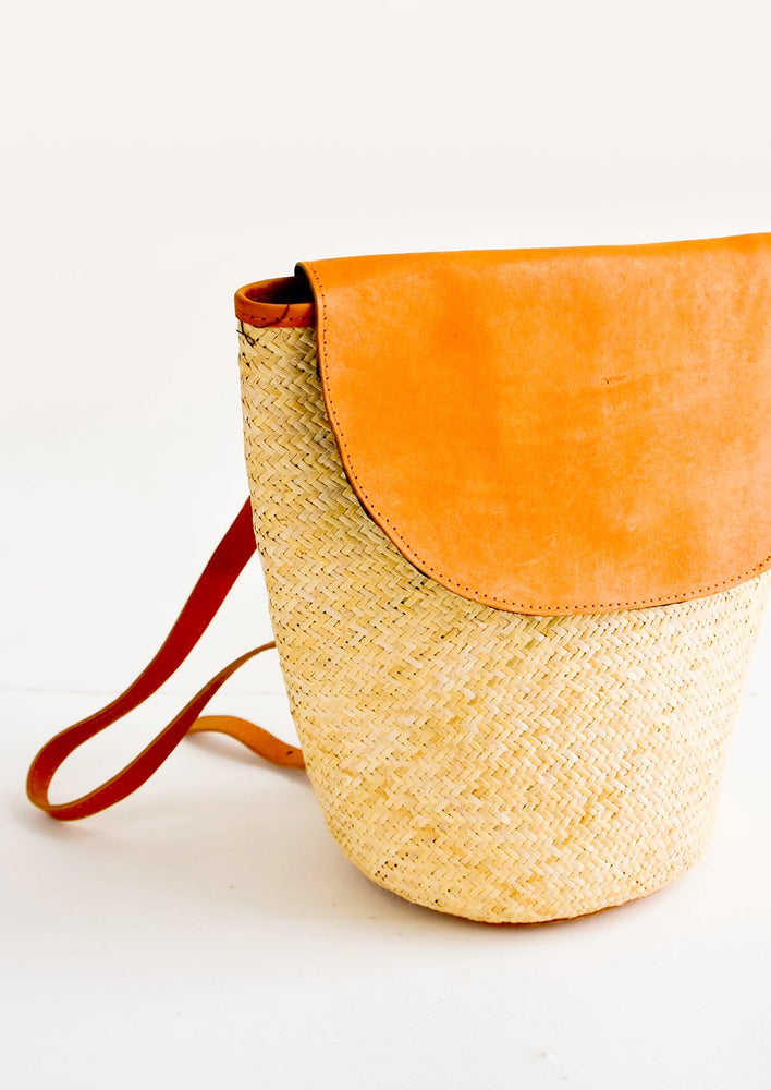1: Woven straw backpack with leather trim and curved front flap
