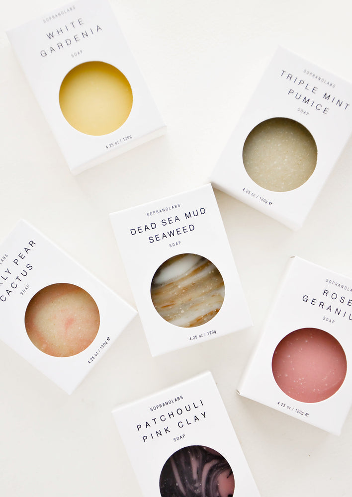 Six bar soaps laid out in white packaging with circular cutouts to show their various colors and textures.