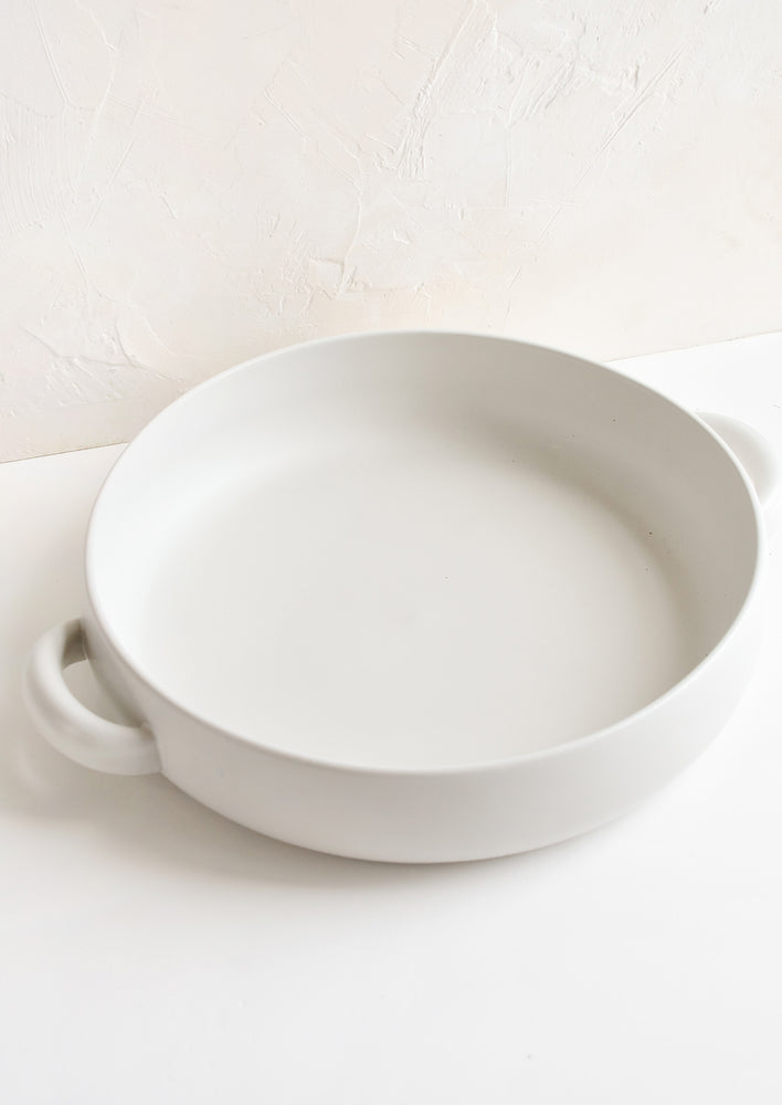 1: A round, shallow extra large serving bowl in white ceramic with curved handles at sides.